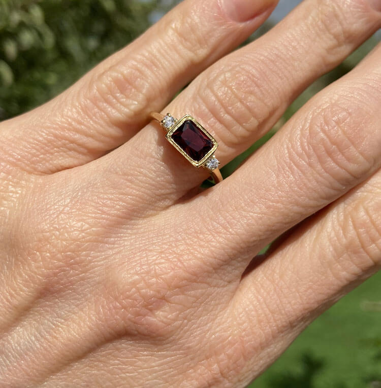 This gorgeous and elegant women's ring features an octagon-cut natural garnet gemstone with two round-cut dazzling clear quartz. This beautiful ring is enhanced with a high polish finish.