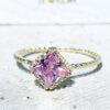 Это великолепное кольцо демонстрирует простую элегантность в своем дизайне. Кольцо украшено драгоценным камнем из розового кварца квадратной огранки и украшено тонкой перекрученной лентой.