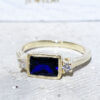Dieser wunderschöne und elegante Damenring ist mit einem blauen Saphir-Edelstein im Achteckschliff und zwei blendend klaren Quarzen im Rundschliff besetzt. Dieser schöne Ring ist mit einem Hochglanz-Finish veredelt.