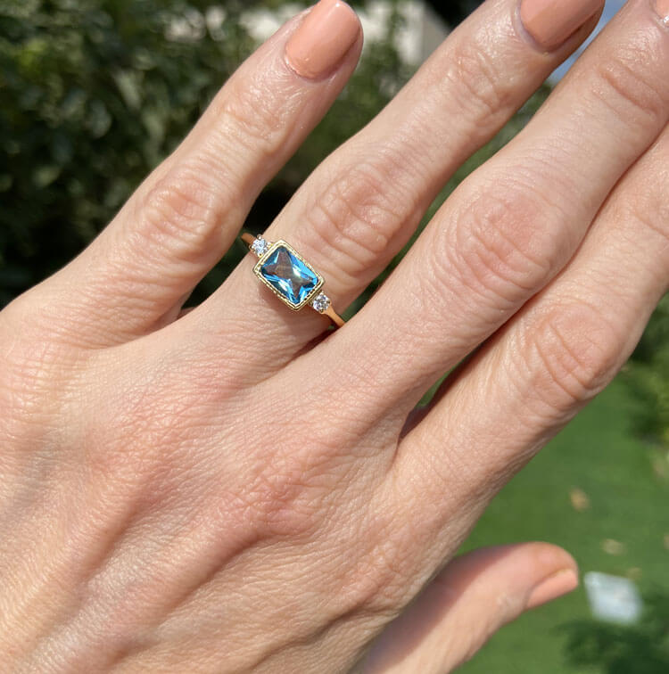 Dieser wunderschöne und elegante Damenring ist mit einem blauen Topas-Edelstein im Achteckschliff und zwei blendend klaren Quarzen im Rundschliff besetzt. Dieser schöne Ring ist mit einem Hochglanz-Finish veredelt.
