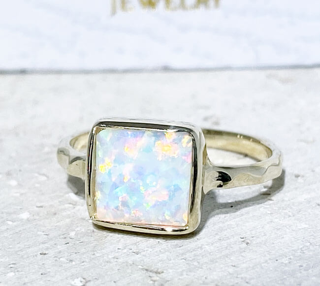 This gorgeous opal ring displays simple elegance in its design. The ring features a square-cut white opal gemstone and finished with a hammered band.