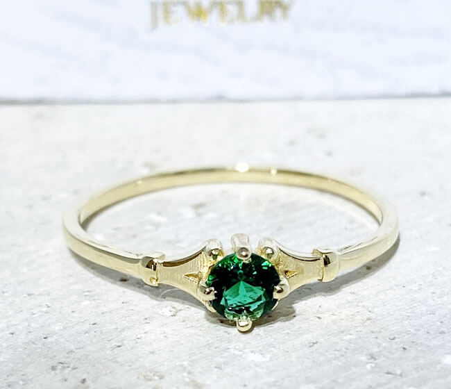 This gorgeous emerald ring displays simple elegance in its design. The ring features a round-cut emerald gemstone and finished with a delicate band.