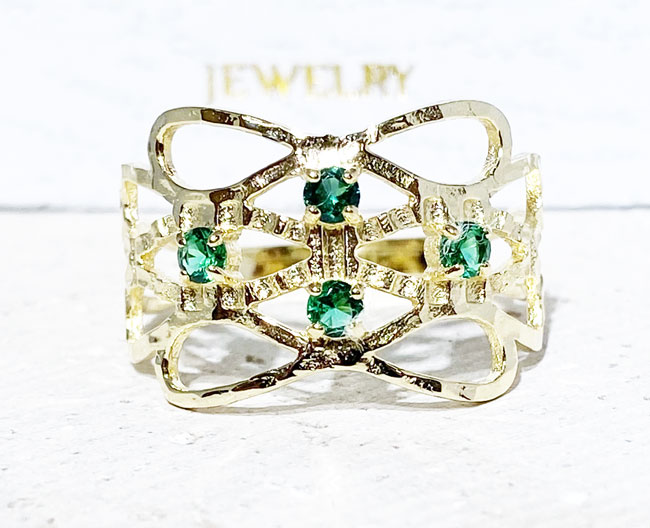 This gorgeous emerald ring displays simple elegance in its design. The ring features a round-cut emerald gemstones and finished with a hammered band.