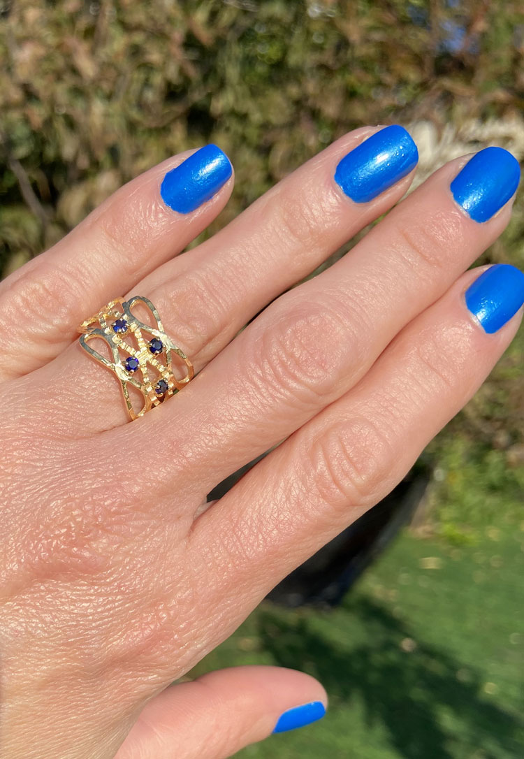 This gorgeous sapphire ring displays simple elegance in its design. The ring features a round-cut blue sapphire gemstones and finished with a hammered band.